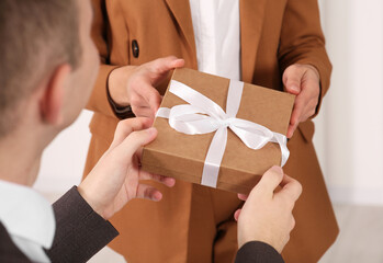 Woman presenting gift box to his colleague indoors, closeup