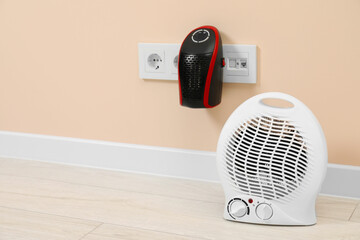 Modern electric compact and fan heaters indoors, space for text