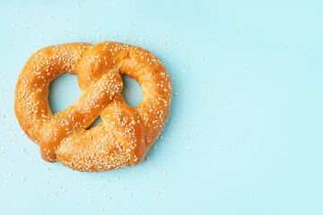 Tasty pretzel with sesame seeds on color background
