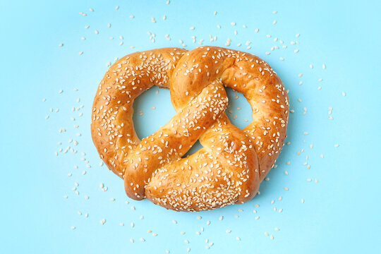 Tasty pretzel with sesame seeds on color background