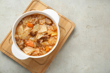 Tasty cabbage soup with meat and carrot on light grey textured table, top view. Space for text