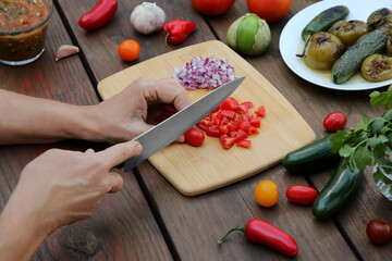 Woman cutting tomato for salsa sauce at wooden table, closeup