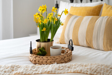 Cheerful yellow flowers and tea on a tray in a stylish bedroom - 584499352