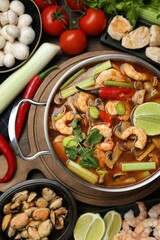 Saucepan with delicious Tom Yum soup and ingredients on wooden table, flat lay