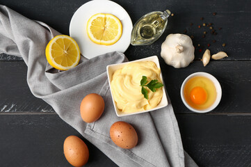 Bowl with tasty mayonnaise sauce and ingredients on dark wooden background