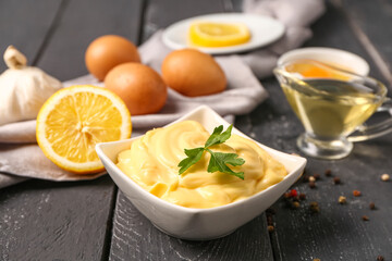 Bowl with tasty mayonnaise sauce and ingredients on dark wooden table