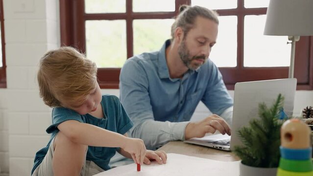 Father sitting at work using tablet while son drawing and painting, family relations concept
