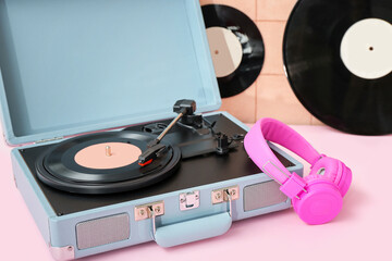 Record player with vinyl disk and headphones on table near beige tile wall