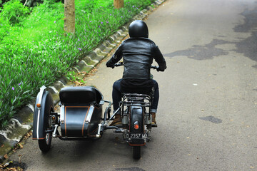 Man riding a black classic European motorcycle on the road in the mountains.