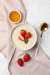 Bowl of tasty semolina porridge with strawberry on light grunge background