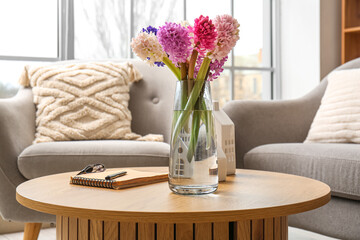 Vase with beautiful hyacinth flowers and notebook on coffee table in modern living room