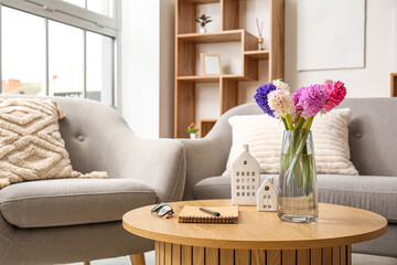 Vase with beautiful hyacinth flowers, glasses and notebook on coffee table in modern living room