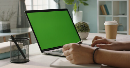 Close up shot of hands of student working with chroma key green screen laptop, using trackpad and pen with notebook in living room - technology concept