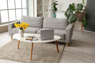 Interior of stylish living room with modern laptop and flower vase on coffee table