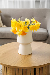 Vase with beautiful narcissus flowers on coffee table in cozy living room