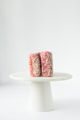 Pink lamingtons on a white marble cake stand Australian raspberry lamingtons, small cakes covered in desiccated coconuts