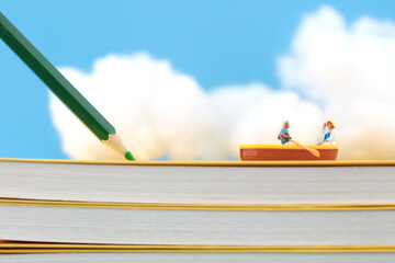 Miniature concept rowing book with colored pencils and white clouds