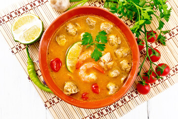 Soup Tom Yum with lime in bowl on light board top