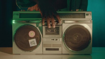 Close-up zoom shot of man inserting cassette tape in retro boombox and turning on the music in the studio with neon light