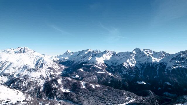 Aerial reveal of snow covered mountain landscape with forests on a sunny winter day in Alp Grum, Switzerland.