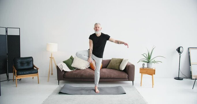 Mature man practices yoga tree pose to train balance