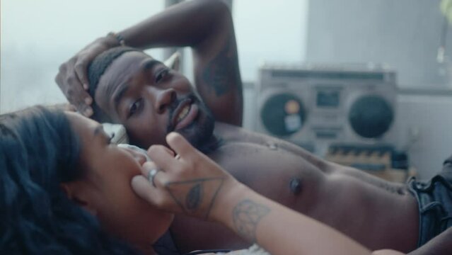 Young romantic couple resting together on bed, chatting, sharing a cigarette and relaxing at home. Racking focus shot