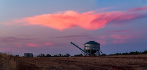 Pink sunset clouds behind the silhouette of a temporary storage grain shed
