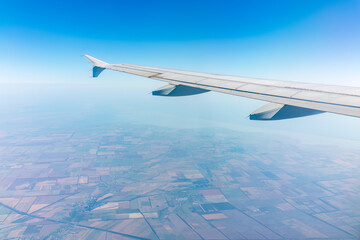 Fototapeta premium Aerial view from airplane window above green ground. View from the airplane window with beautiful clouds at sunrise