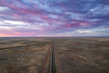 The sky is filled with pink storm clouds as the camera looks down on a remote road with dirt tracks on either side