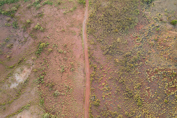 Looking down on a red earth dirt speckled with green bushes over the land.
