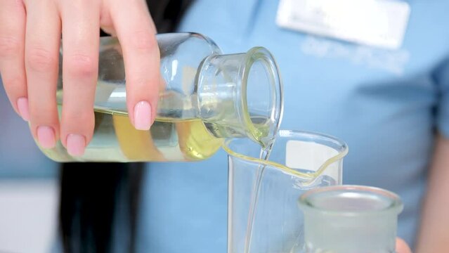 Closeup professional scientist pours clear yellow liquid extracted from oil into lab glass in refinery factory laboratory. High quality 4k footage