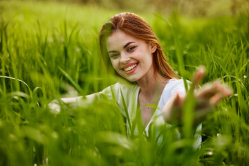 portrait of a broadly smiling woman sitting in tall grass and holding out her hands to the camera