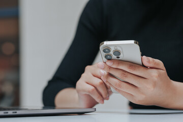 Young Asian woman using smartphone and laptop working remotely at coffee shop.