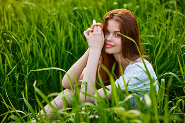 cute woman in summer high grass sits in a light dress