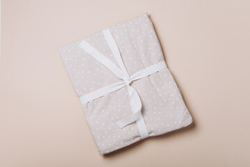 Stack of clean bed sheets with bow for present or gift on beige background. Top view. Copy space