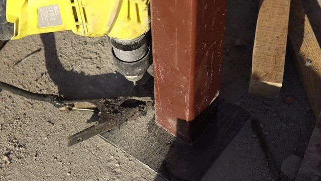 The builder with hammer drill perforator equipment making hole in wall at construction site