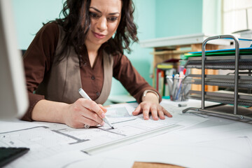 Beautiful architect at her working desk with blueprints in front of her. Working on new projects. Architecture and design