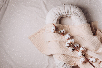Beige cocoon, baby nest for newborn, blanket, cotton flowers over cribs in nursery. Childhood...