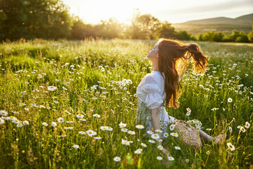 a red-haired woman in a light dress sits with her back to the camera in a field of daisies...