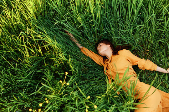 a relaxed woman enjoys summer lying in the tall green grass in a long orange dress stretched out stretching her arm forward