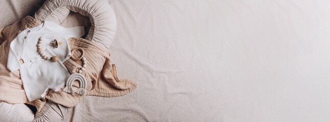 Girl romper, leggings, head bow, pacifier holder, bib, teether, crocketed toy over beige cocoon, nest. Baby clothes, accessories, toys set on neural background. Fashion newborn essentials. Top view