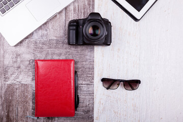 Over top photo of camera, laptop, writing notebook and sunglasses on wooden background