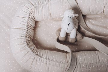 Soft sheep toy on beige cocoon, baby nest for newborn over cribs in nursery. Childhood concept....