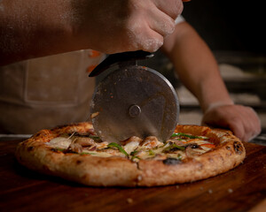 Man's hand holding cutter over hot italian pizza on the grey marble background.