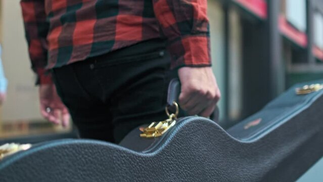 Up close shot of a guitar case being held by a musician.