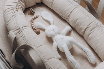 Soft rabbit toy on beige cocoon, baby nest for newborn over cribs in nursery. Childhood concept....