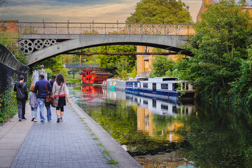 Fototapeta premium Family waking along Regent's Canal in London, England, at sunset in the summer; bridge in background; marooned barges reflect in calm water