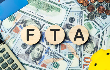 FTA text in wooden circle on Banknotes background, credit card, piggybank, calculator. Free trade agreement, planning goals, opportunity, challenge, Budget, business strategy and financial concept.