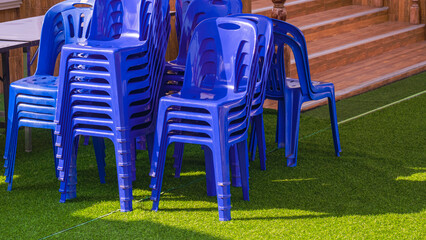Group of blue plastic chairs and foldable table on green artificial turf outside of building for...