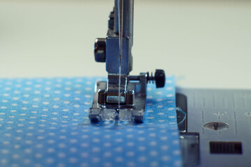 Detailed close up shot of sewing machine steel foot with needle and thread stitching on blue fabric polka dot textile. Sewing machine, tailor's shop, atelier, dressmaker industry. Needle craft